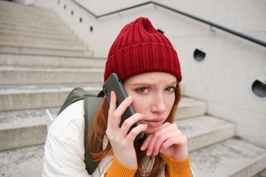 Redhead girl with concerned face, looking worried while answering phone call, hears bad news over telephone conversation, rings someone with upset emotion