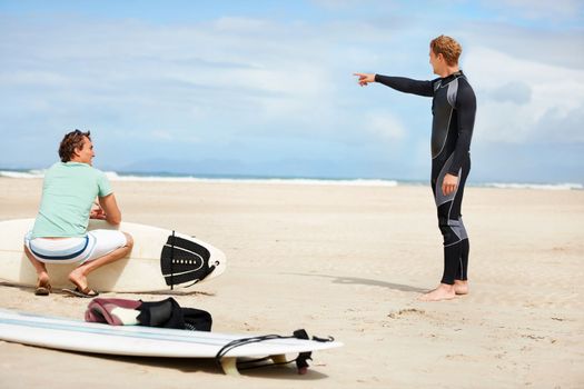 Time to hit the waves. A surfer pointing towards the ocean while his friend sits holding a surfboard.