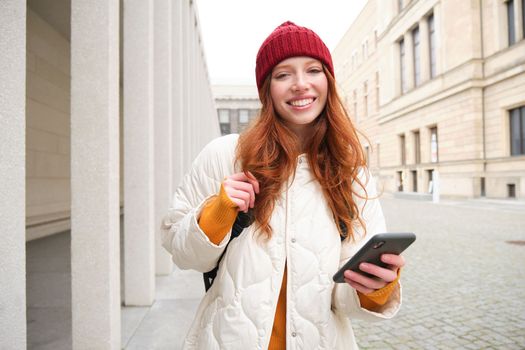 Tourism and technology. Beautiful redhead girl tourist, looking for a route on application, using city map on smartphone, reading about sightseeing places on mobile phone