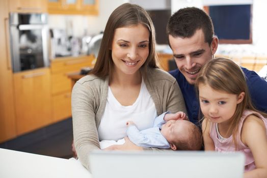 Technology is an important part of their family. A young family gathered around their laptop.