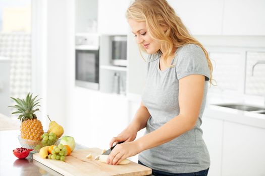 Making the perfect fruit salad. Attractive curvaceous young woman chopping fruit in her kitchen.