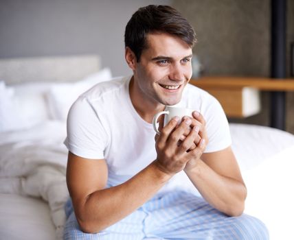Enjoying some freshly brewed coffee. a handsome young man drinking coffee on the edge of his bed.