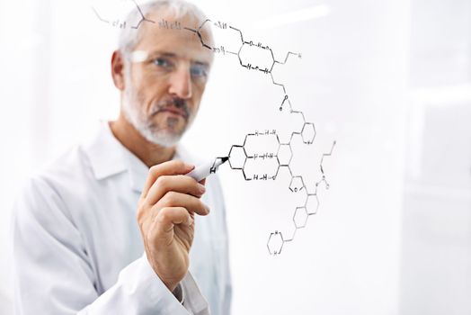 He just knows how they all fit together. a mature male scientist drawing molecule structures on a glass surface.