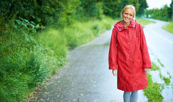 Walking the country roads on a rainy day. Gorgeous young blonde woman wearing a red raincoat in the rain outdoors on a country road.