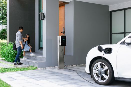 Progressive dad and daughter charging EV car from home charging station.