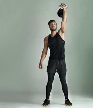 No pain, no gain. Studio shot of a young man working out with a kettle bell against a gray background.
