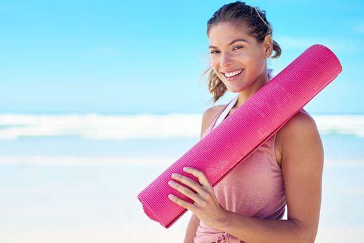 It doesnt have to be yoga OR the beach. a young woman holding a yoga mat while standing on the beach.
