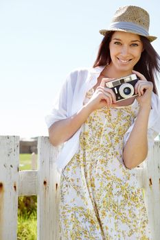 Picture perfect. A beautiful young woman standing outside with a vintage camera.