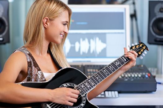 Making the strings sing. A beautiful blonde woman playing her guitar in a recording studio.