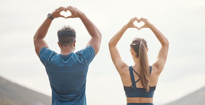 Fit young man and woman from the back gesturing heart shapes with hands while exercising together outdoors. Two athletes caring for body with regular training workout or run. Endorsing and loving a h