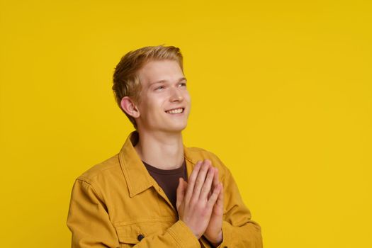 Happiness Gratitude Faith Concept. Smiling Young European Man Joined His Palms in a Gesture of Gratitude on a Yellow Background.