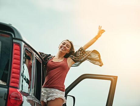 Freedom is the best feeling. Portrait of a young woman leaning out a car with her arms outstretched while on a roadtrip.