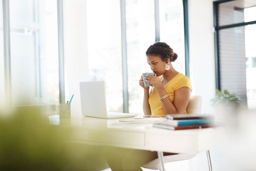 Coffee breaks are for catching up on social media. a young businesswoman using a laptop and drinking a beverage at her desk in a modern office.