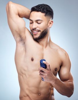The ladies love a man that smells good. a young man applying deodorant against a studio background.