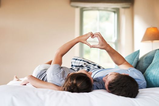 We complete each other in everywhere. an affectionate young couple making a heart shape with their hands in their bedroom at home.