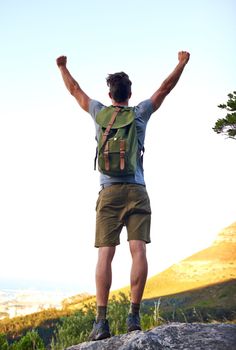 He made it. a handsome young man standing with his arms raised while hiking.