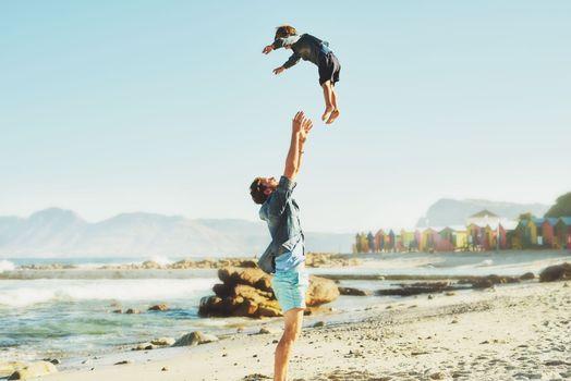 Let the sea set you free. a young Father tossing his son into the air at the beach