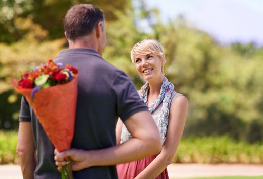 I have a surprise for you. a mature man hiding a bouquet of flowers from his girlfriend behind his back.