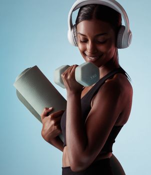 Yoga, dumbbell and woman in studio training strong biceps in exercise with headphones for music streaming. Fitness, healthy and happy girl listening to audio, radio and lifting weights for arm power