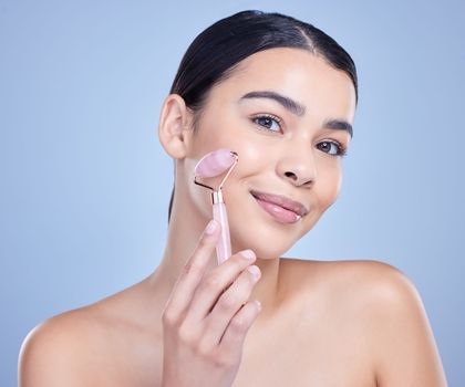 Studio Portrait of a beautiful mixed race woman using a rose quartz derma roller during a selfcare grooming routine. Young hispanic woman using anti ageing tool against blue copyspace background