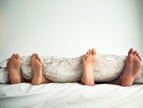 Lets cancel today and stay in bed. a couples feet poking out from under the bed sheets.