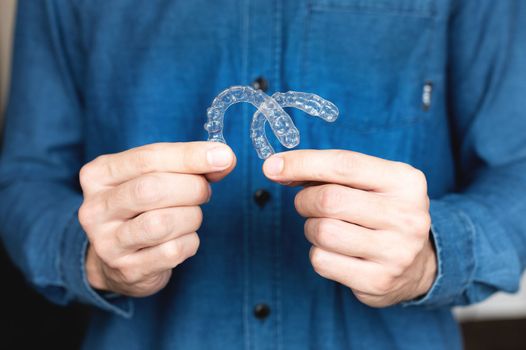 close-up of a young man, holding an invisible tooth alignment retainer in his hands. beautiful teeth orthodontic health concept