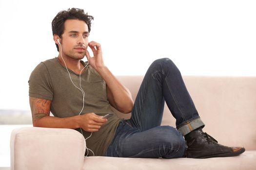 Relaxing with his tunes. A handsome young man listening to music on his mp3 player isolated on white.