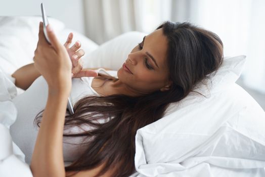 Connected in comfort. a beautiful young woman relaxing in bed with her tablet.