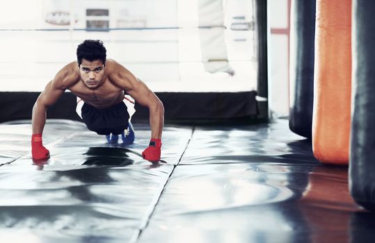 Boxing is a way of life. A focused young boxer doing push-ups in the gym.