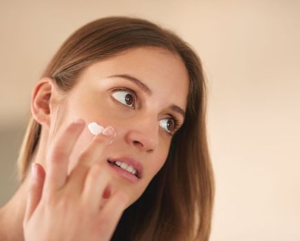 Giving her skin the nourishment it needs. a young woman applying moisturiser to her face.