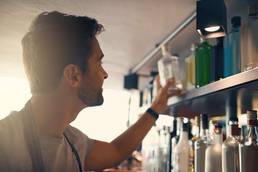 The talent behind a great drink. a young man looking at the merchandise on the shelves behind a bar counter.