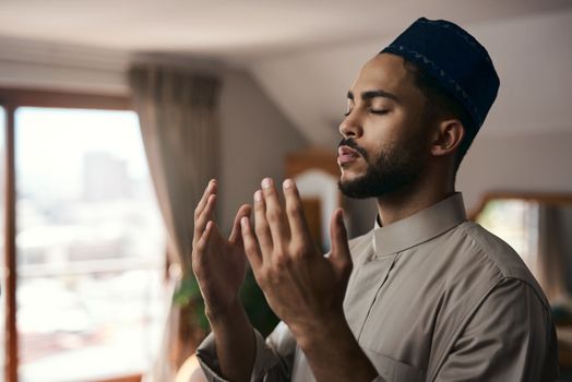 Prayer is the song of the heart. a young muslim man praying in the lounge at home.