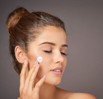 Beautiful skin begins with exceptional skincare. a youthful model applying moisturizer to her face in studio.