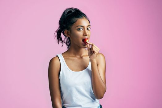 This ones all mine. Studio portrait of a beautiful young woman eating a strawberry against a pink background.
