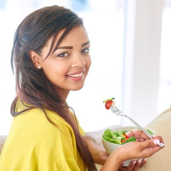 Staying on the healthy side. a young woman eating a salad at home.