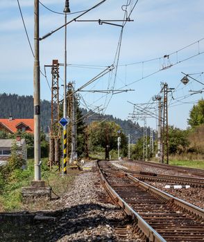 Empty railway tracks on a sunny summer day, in rural area, pillars with many electric cables around.