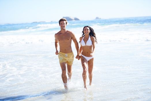 Enjoying the sunshine. A happy couple in swim wear running on the beach together.