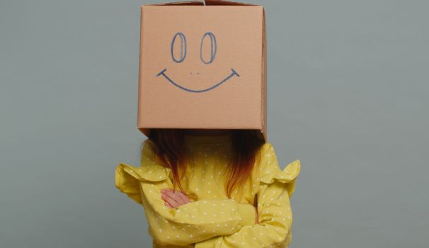 Preteen child kid frustrated after quarrel, wearing cardboard box with smiling face to change mood