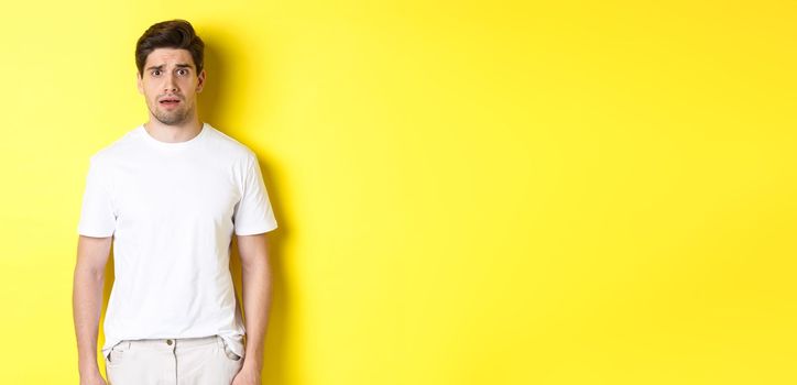 Image of confused and nervous man looking at something strange, frowning anxious, standing against yellow background