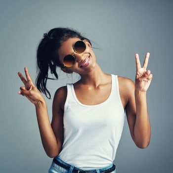Peace to all. Studio portrait of a beautiful young woman giving you two peace signs against a grey background.