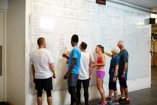 Working towards their goals. Rearview shot of a group of people looking at a whiteboard while standing in the gym.