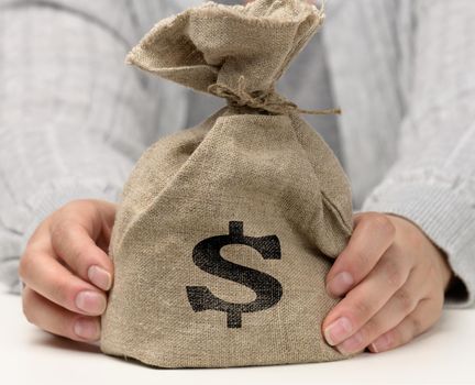 hand holds a canvas bag full of money with a US dollar icon on a white background