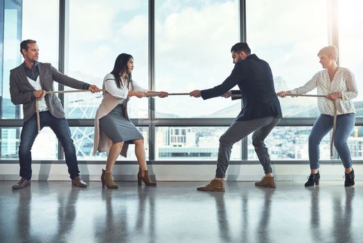 The business world is quite a competitive one. a group of businesspeople pulling on a rope during tug of war in an office.