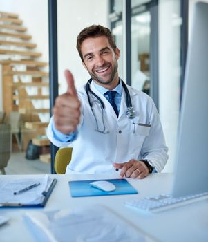 Im glad to see youre looking better. Portrait of a young doctor showing thumbs up while working in his office.
