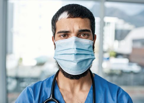 Hes had to carry the responsibility and risk. Portrait of a medical practitioner wearing a face mask in a hospital.