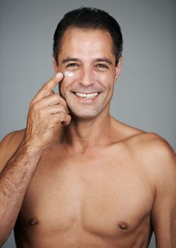 Applying his warpaint- its a battle against aging. Studio shot of a handsome mature man applying moisturizer to his skin.