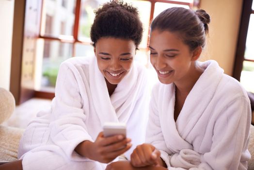 Status update Pure bliss. two friends in bathrobes using a cellphone at a spa.