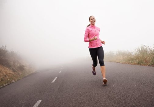 Peeling off the miles. a young woman jogging on a country road on a misty morning.