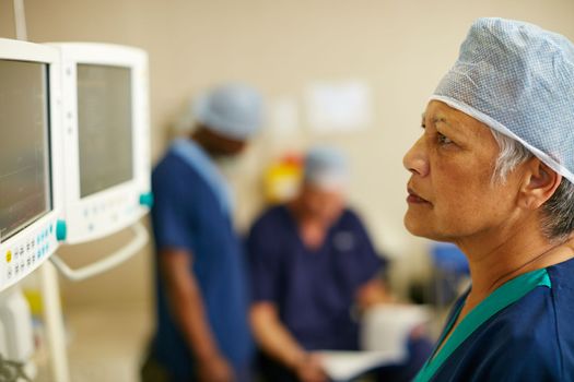 Keeping a close eye on her patients vitals. a surgeon looking at a monitor in an operating room.
