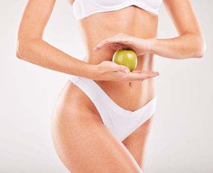 Wellness, diet and hands with apple for slim body, self care and healthy lifestyle on white background studio. Fitness, exercise and abdomen of woman with fruit for vitamins, nutrition and weightloss